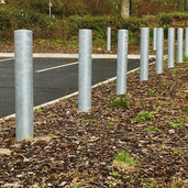 Gegalvaniseerde stalen parkeerpalen (Ø102 mm) langs een parkeerplaats, verankerd in de grond.